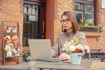 Beautiful woman traveler on the street of the old city. Business lady sits at a table in a summer cafe and works at a computer