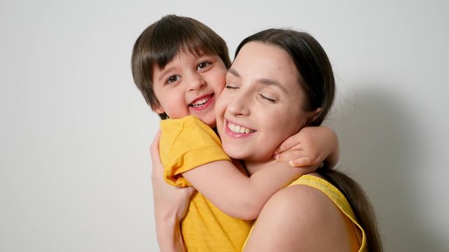 boy hugs his mom tightly dressed in yellow poppies against a white wall in the studio