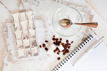 A cup of coffee, chocolate, a sheet of paper and a pen on a white wooden surface. Background for work at home in quarantine. The difficulty of adapting work at home.