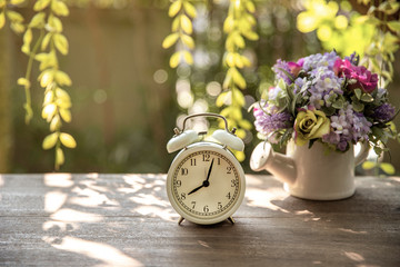 flower bouquet in white vase with vintage alarm clock on wooden table in nature background with...