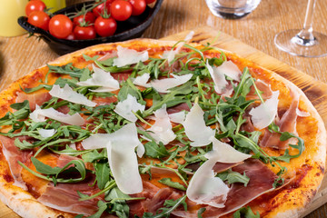 Fresh oven baked traditional prosciutto, rucola, tomato and parmesan pizza, served on a wooden board