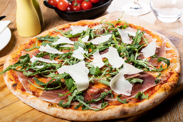 Fresh oven baked traditional prosciutto, rucola, tomato and parmesan pizza, served on a wooden board