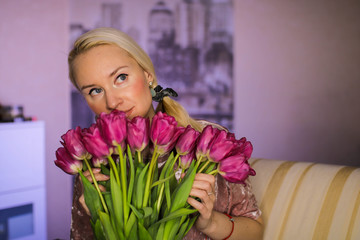 Beautiful young blond woman with tulip bouquet. Spring portrait. At home. Interior. Mother's Day.