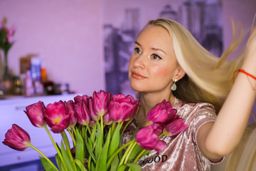 Studio shot of beautiful woman holding red tulip flowers and smiling while looking aside, happy model posing isolated over blurred neon background.
