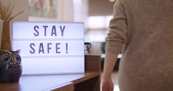 Woman walks in and Switches on Decorative Lightbox Written Stay Safe in Comfy and Cozy Home