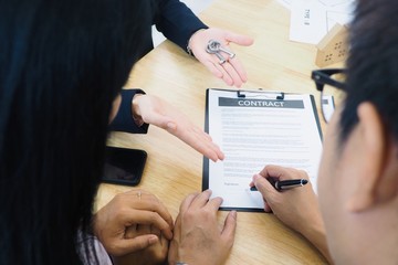 Clients signing contract of buying a new property at a real estate company. Agent giving keys and providing home loan and financial planning information. 