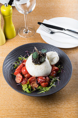 Burrata cheese pouch sack on top of cherry tomatoes salad and rucola arugula leaves, olive paste