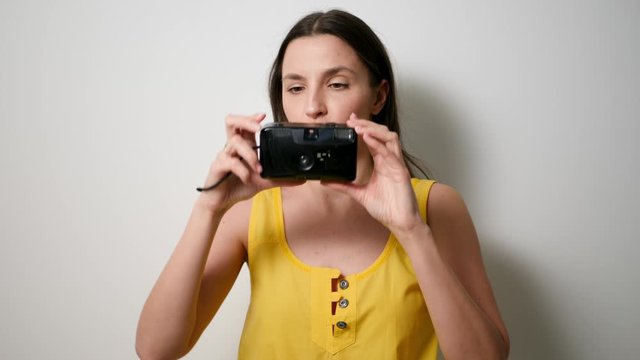 girl photographer in a yellow t-shirt takes a soap dish on an old plastic camera while standing against a white wall in a studio