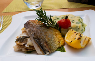 White fish fillet with puree served with lemon and rosemary in a white plate, restaurant setting