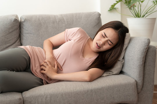 Asian women with menstrual pain at abdomen And the face expression. Asia woman having painful while lying on the sofa at her home