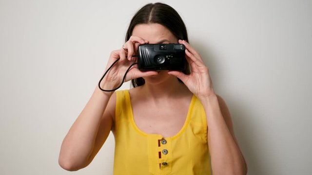 girl photographer in a yellow t-shirt takes a soap dish on an old plastic camera while standing against a white wall in a studio