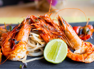 Sauteed shrimps in tomato, capers and olives sauce. Black plate in a restaurant setting background