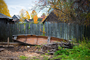 An old wooden abandoned boat on the ground and dilapidated village buildings around