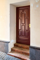 Wooden elegant entrance door with stone red granite threshold and steps at the facade of the building with peeling plaster.