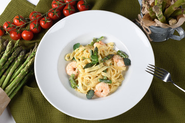 Tagliatelle or pappardelle pasta with asparagus and shrimps, cherry tomatoes in the background.