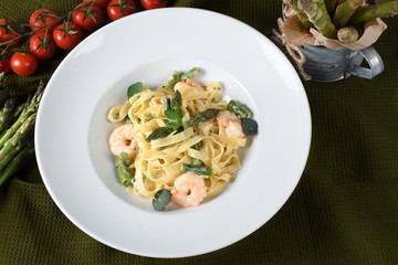 Tagliatelle or pappardelle pasta with asparagus and shrimps, cherry tomatoes in the background.