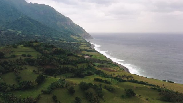 Aerial shot of a mountain beside the sea with strong waves crashing on the beach on a cloudy day