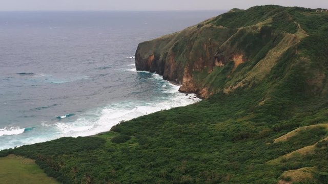 Aerial shot of strong sea waves crashing to a rocky beach and the tall cliffs beside it