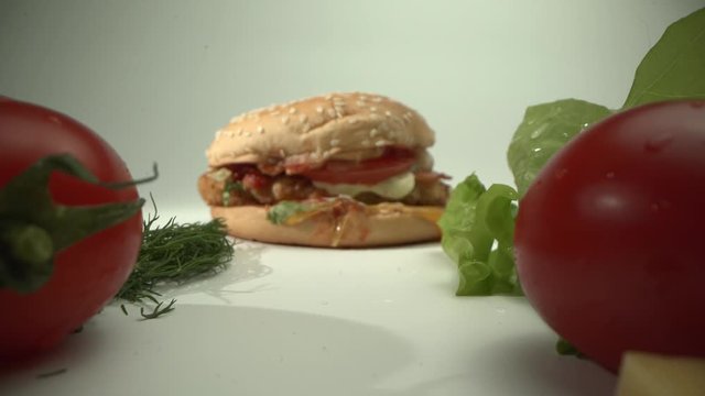 The camera moves past tomatoes, cheese and herbs to a delicious hamburger.