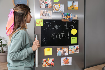 Young woman opening refrigerator in kitchen