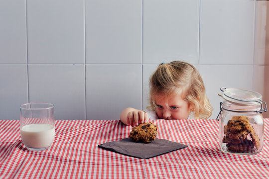 blonde girl taking a cookie off the table.