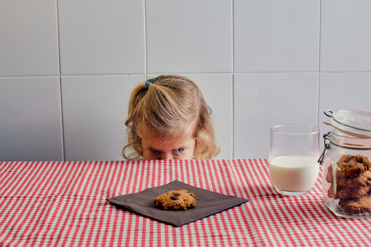 girl poking her head above the table looking at a cookie