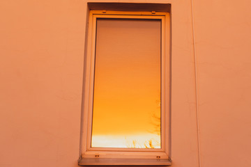 The golden glare of the sun on the window of a house during sunset