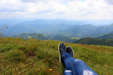 Woman hiker in blue jeans lies on the green grass on the top of Hoverla Mountain in the Carpathians in summer.