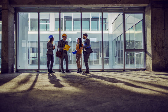 Four dedicated hardworking architects standing next to big window in and old building and talking about how they plan to rebuilt it to be modern.