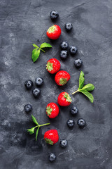 Naklejka na ściany i meble Composition of strawberries and blueberries and mint leaves on a dark concrete background top view
