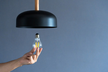 Close-up. A hand changes a light bulb in a stylish loft lamp. Spiral filament lamp. Modern interior...