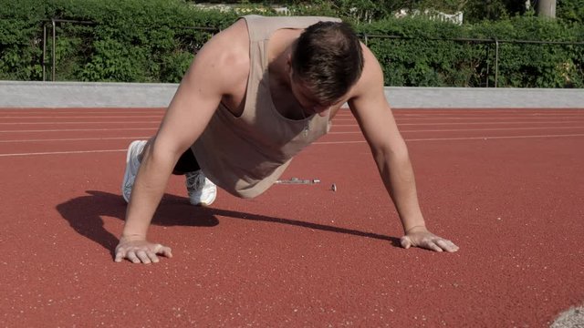 Muscular bodybuilder doing pushups on a race track before running