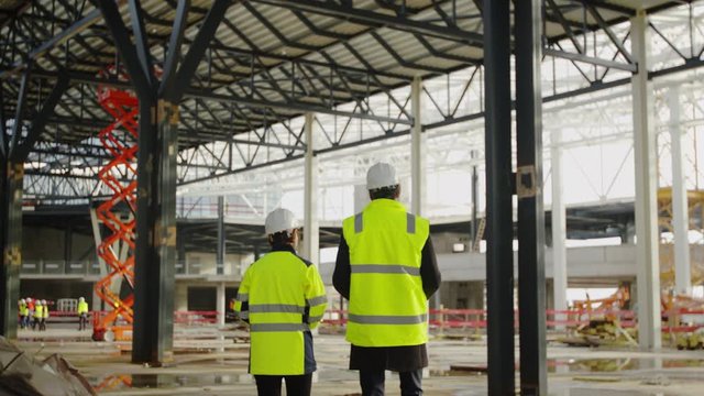 Rear view of engineers walking on construction site, talking.
