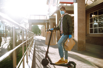 Сourier in medical mask and gloves delivers on a scooter a bag of food in quarantine city. Delivery service concept. Covid-2019.