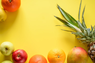 Top view of different tropical fruits by frame on the Yellow background 