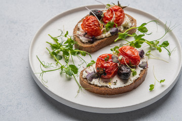 Sandwiches with baked tomatoes, olives, cheese and herbs on bread on a white ceramic plate
