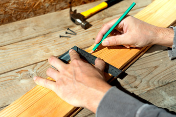 Male carpenter marks with pencil using a square on the board, marks for saw cut. Male hands with pencil and a square close-up on wooden board.