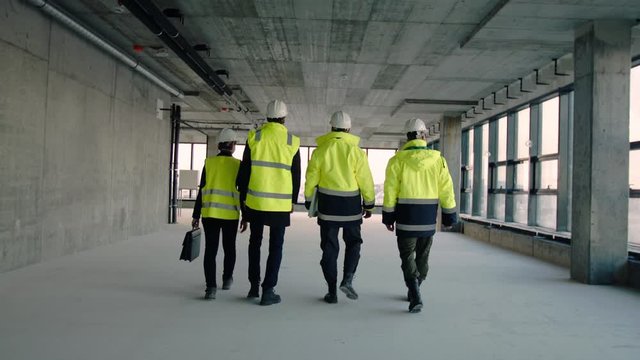 Rear view of group of engineers walking on construction site, talking.