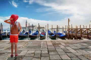 Eine Touristin mit rotem Hut steht am Markusplatz in Venedig, Italien, und schaut auf die Gondeln...