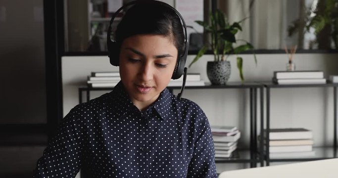 Indian professional customer service support manager, online teacher, secretary wearing headset speaking to distance client, teaching remote student, helping customer in online video conference chat.