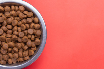 Dog food in a silver bowl. Half of the bowl on the left. Red background. Copy, text sapce.