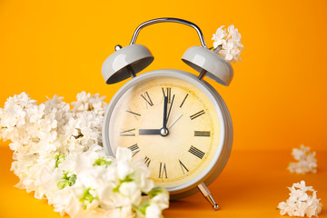 Alarm clock and flowers on color background. Spring time
