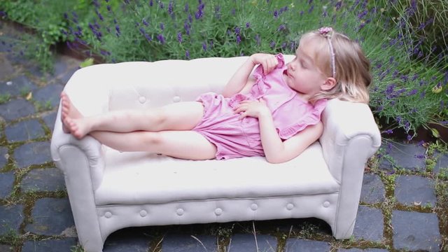 Little blonde lies on a small white sofa in the yard of the house 