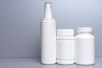 3 plastic containers for medicines and vitamins, a bottle with a spray bottle on a gray background. white cans without a name