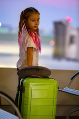 Little girl with pink hair at the airport with a suitcase