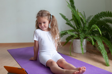 Pretty young girl in sportswear watching online video on laptop and doing fitness exercises at home. Distant training with personal trainer, social distance or self-isolation, online education concept
