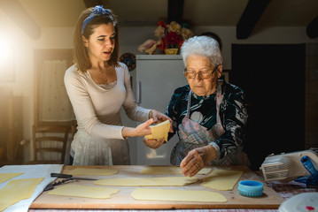 Caucasian grandmother and granddaughter rolling dough for making fresh homemade pasta. Spending time together at home during quarantine. Traditional Italian food. 