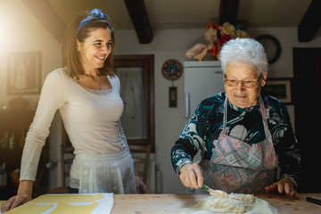 Caucasian grandmother and granddaughter smiling while prepare fresh homemade pasta spending time...