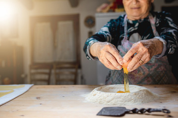 Old woman hands braking eggshell on flour  in a wooden cutting board to prepare some traditional homemade recipe as bread, pasta pastry.