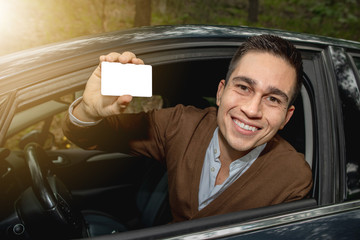 Portrait of young smiling man inside his new car posted outside the window showing the driver...